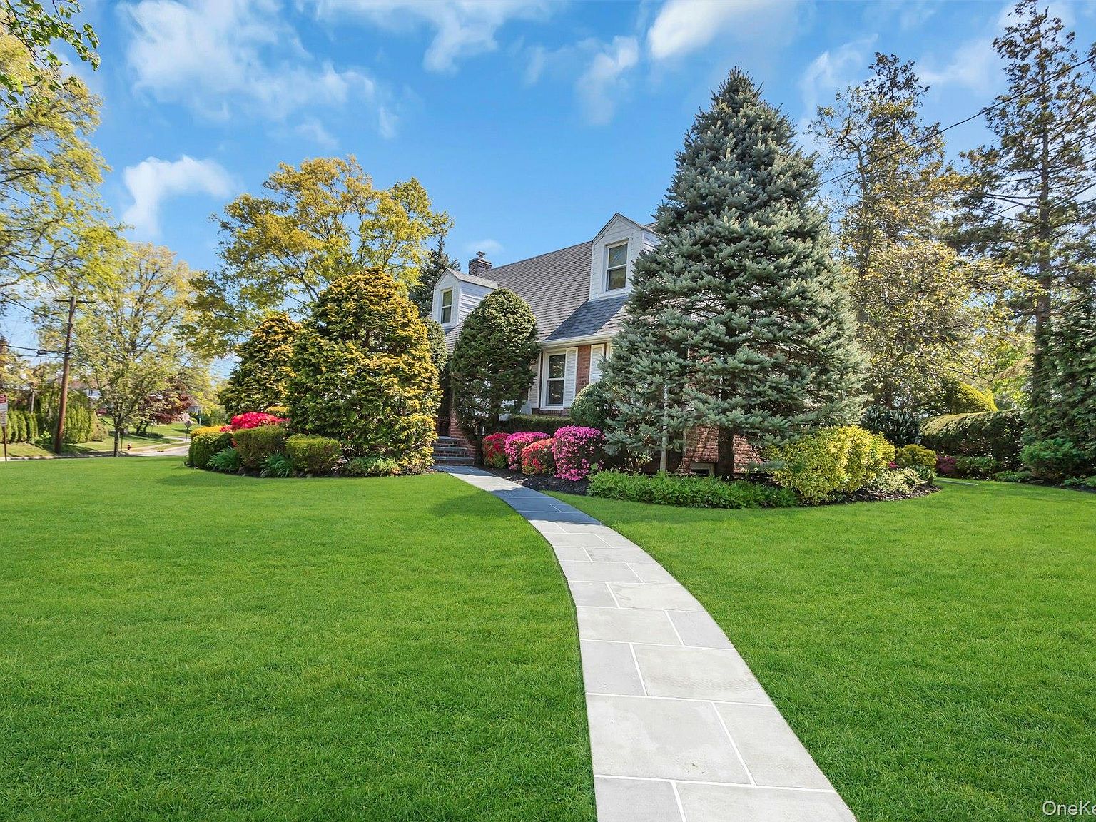 The Cape Cod viewed from the front walk, bordered by mature evergreens and spring blooms
